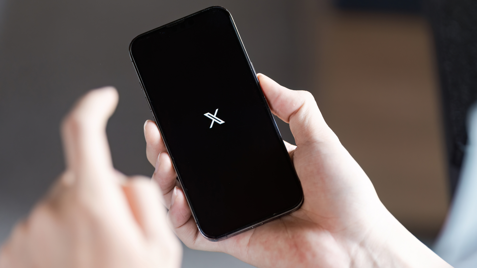 Person holding phone displaying X logo